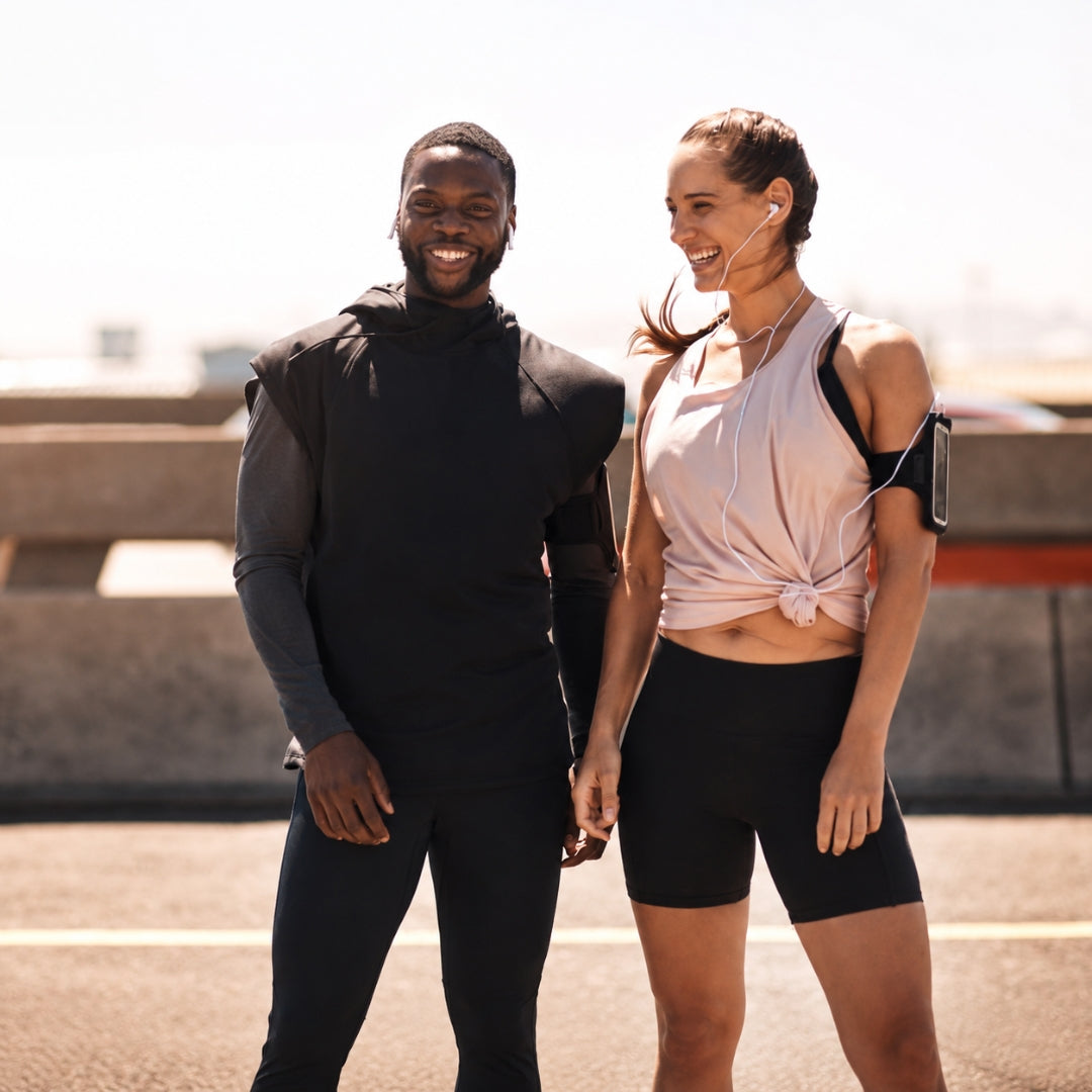 A smiling couple in athletic wear running on a sunny boardwalk.