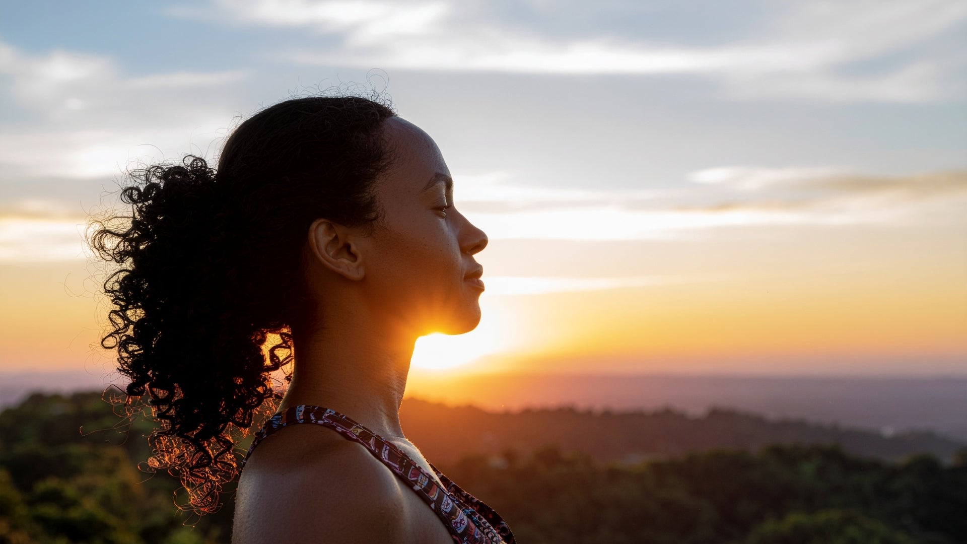 A woman with curly hair meditating peacefully during a beautiful sunset.